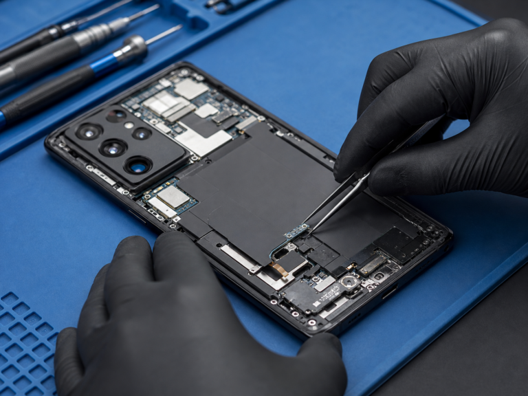 Technician repairing an open Android phone on a blue work mat